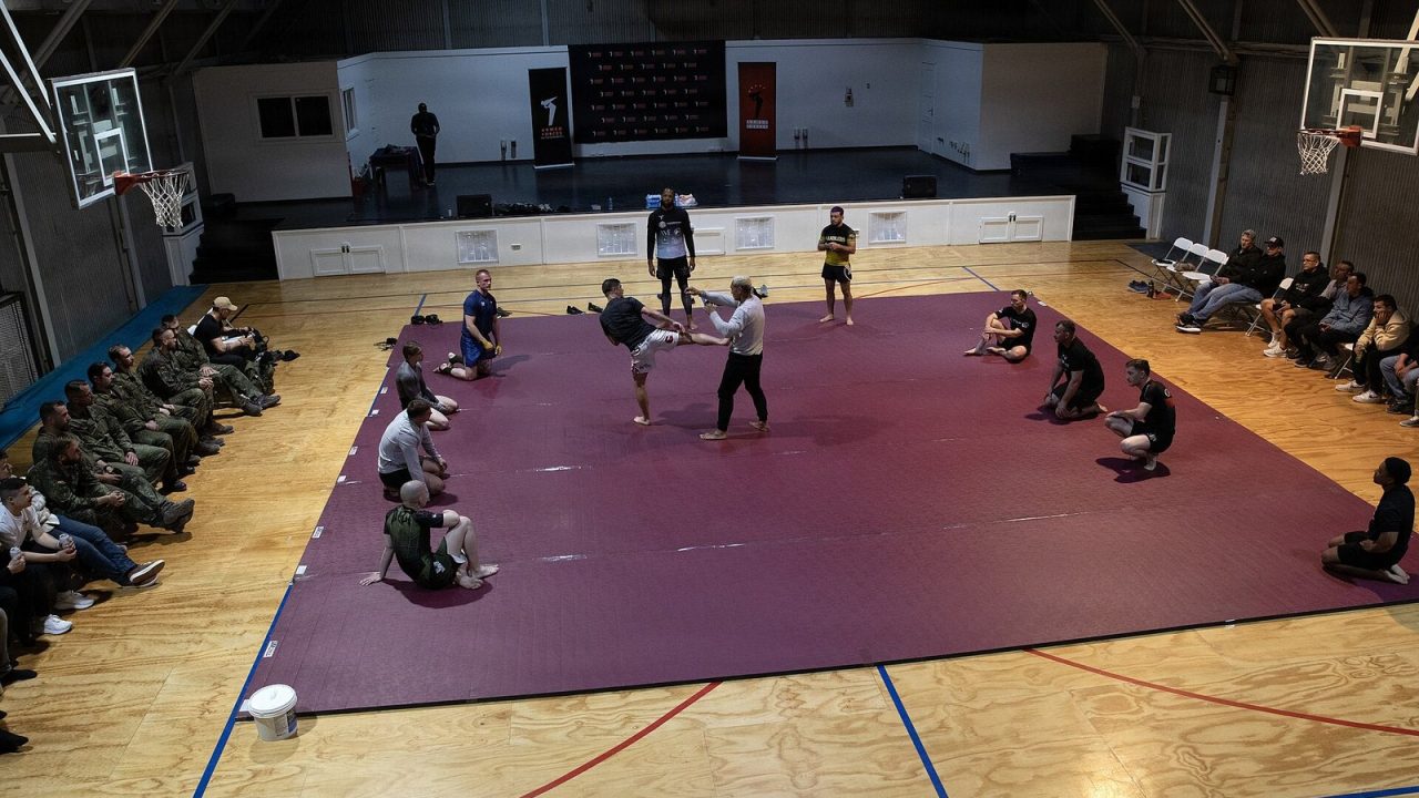 Professional MMA fighters leading a grappling training session on mats for soldiers in Kosovo